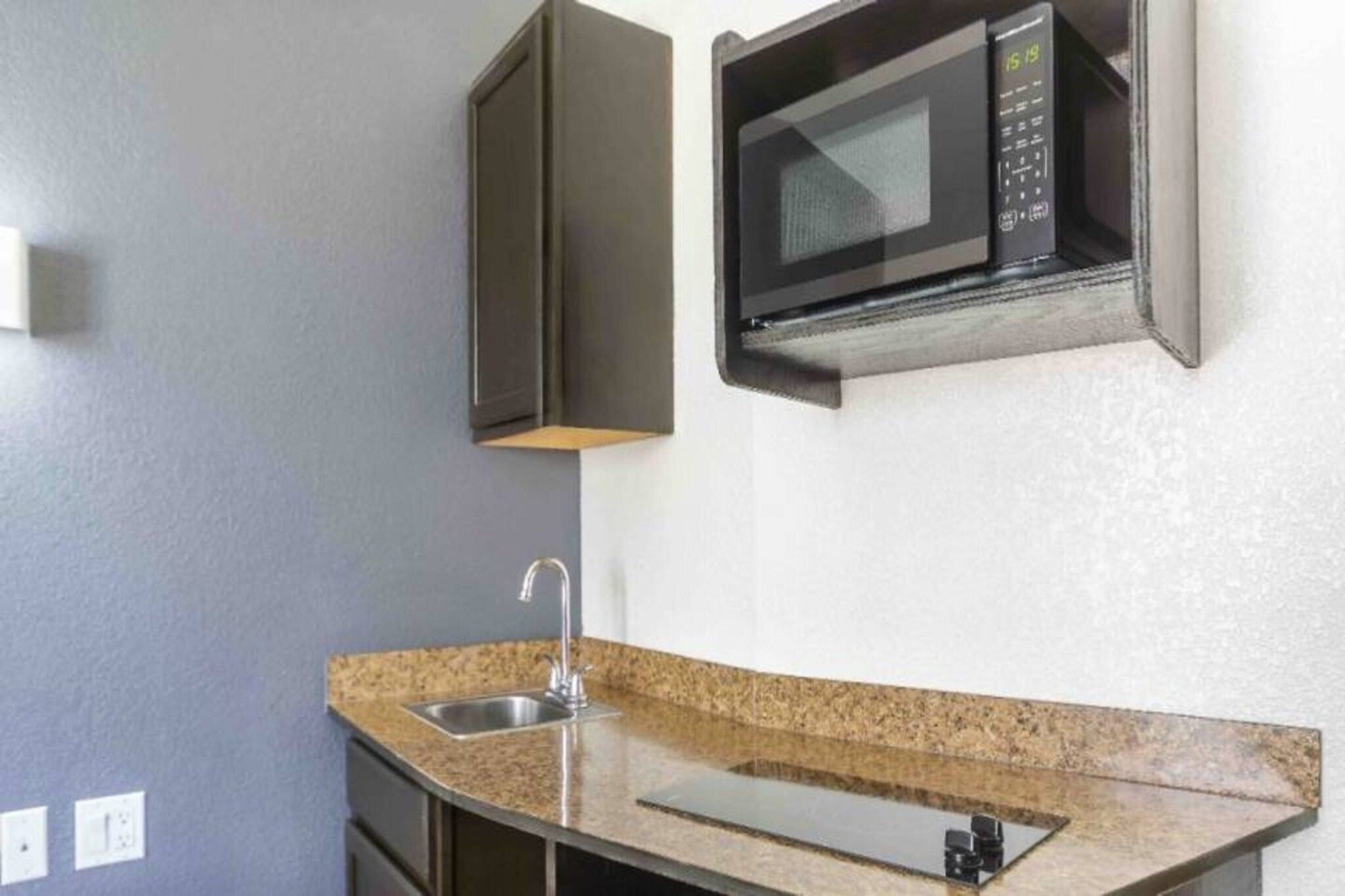 Una cocina con encimera de granito, pileta de acero inoxidable y horno microondas.