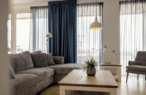 A modern living room with a sectional sofa, a coffee table, a lamp, and a potted plant. - Beach apartment Lobster in Egmond aan Zee for 6 guests, with 3 bedrooms, a terrace and views of the sea and boulevard. (Egmond aan Zee)