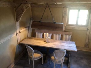 A rustic wooden dining table with two chairs, a hanging light fixture, and a window with blinds. - Holiday Home The old Barn (Schneverdingen)