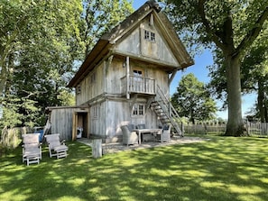 A rustic wooden house with a balcony, a staircase, and a small outdoor seating area with chairs. - Holiday Home The old Barn (Schneverdingen)