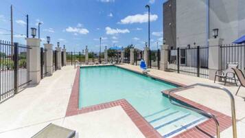A rectangular swimming pool with a tiled edge, surrounded by a fence, and a clear sky above.