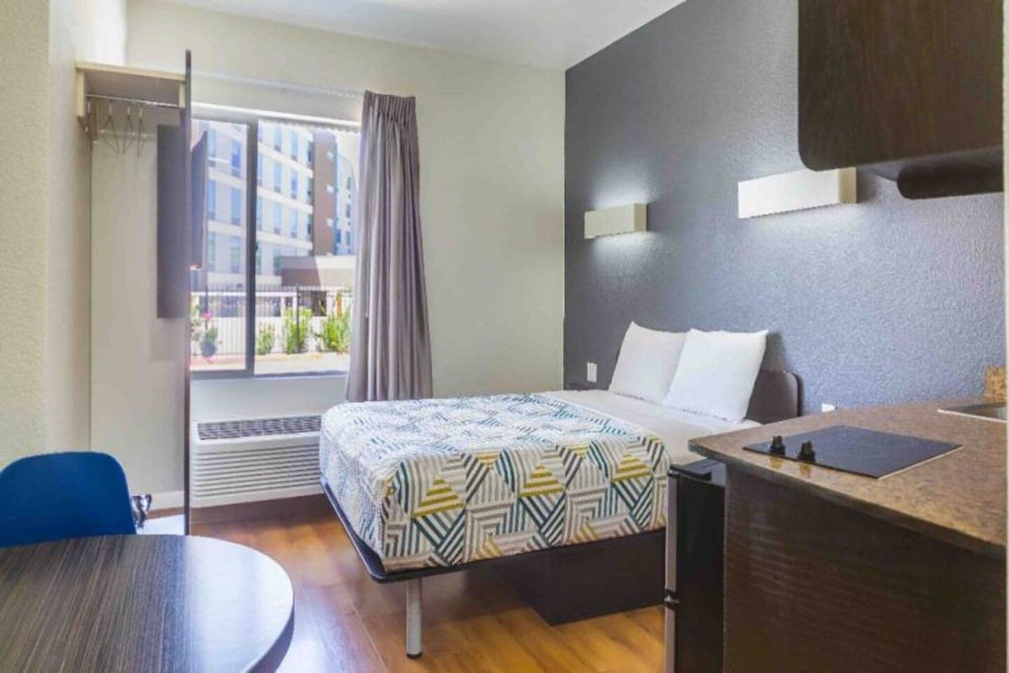 Une chambre d’hôtel avec un lit, un bureau, une chaise, une fenêtre avec des rideaux et une vue sur les bâtiments environnants.
