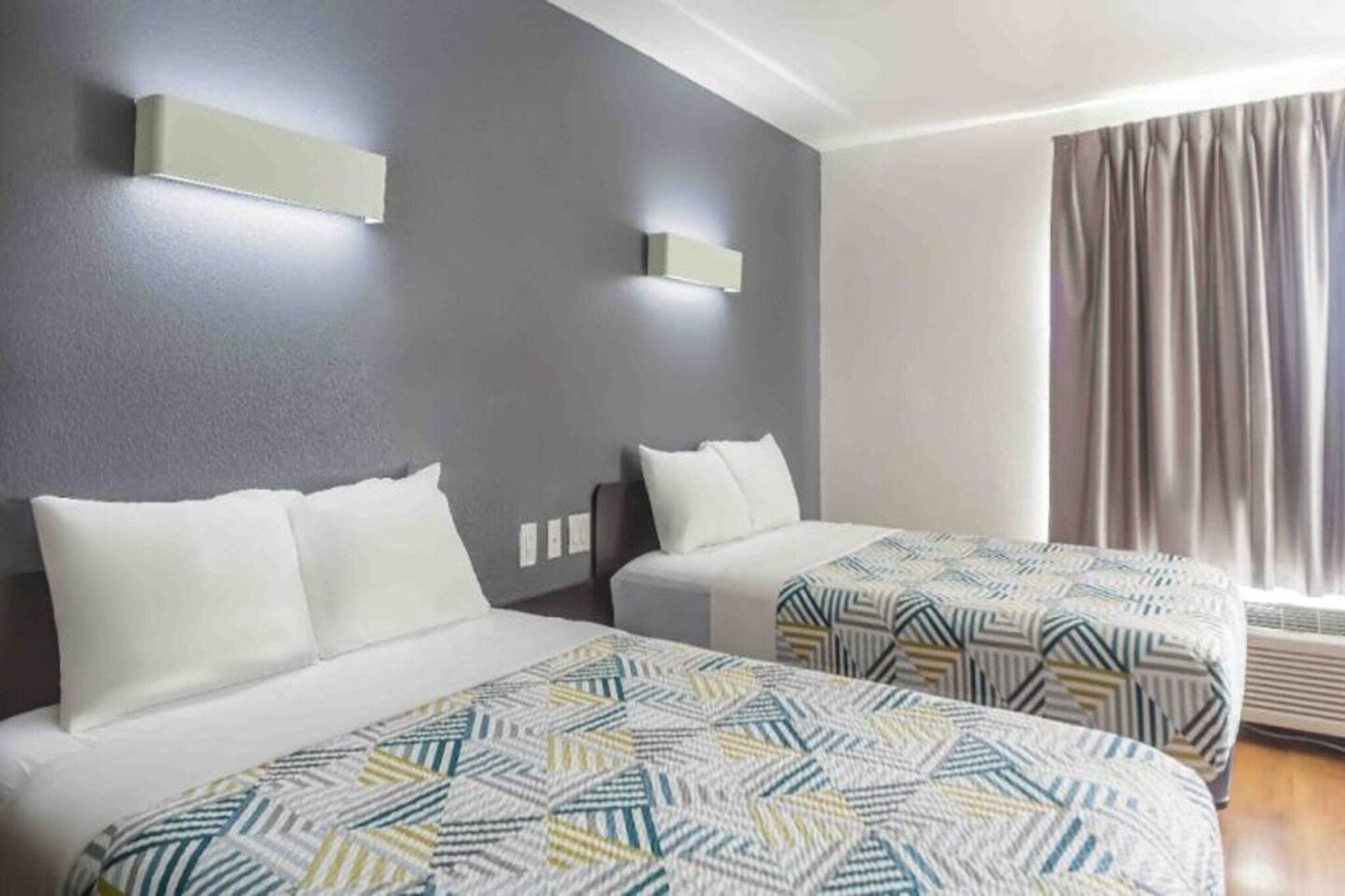 A hotel room with two beds, a grey wall, and a window with curtains.