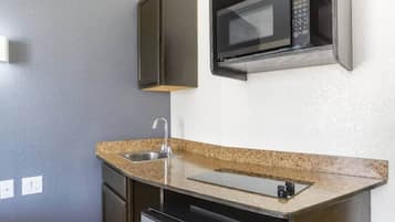 A compact kitchen with a granite countertop, stainless steel sink, and a microwave above it.