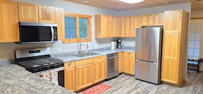 A kitchen with wooden cabinets, a stainless steel refrigerator, a microwave, a stove, and a coffee maker.