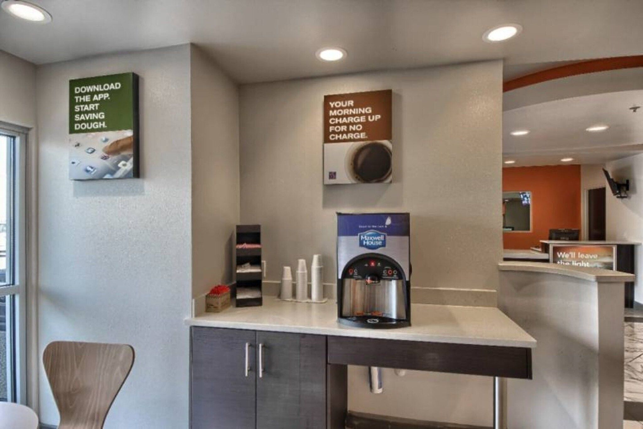 Zona de recepción de un hotel con una máquina de café, un cartel que invita a descargar la aplicación y un aviso sobre el cargo por la mañana.