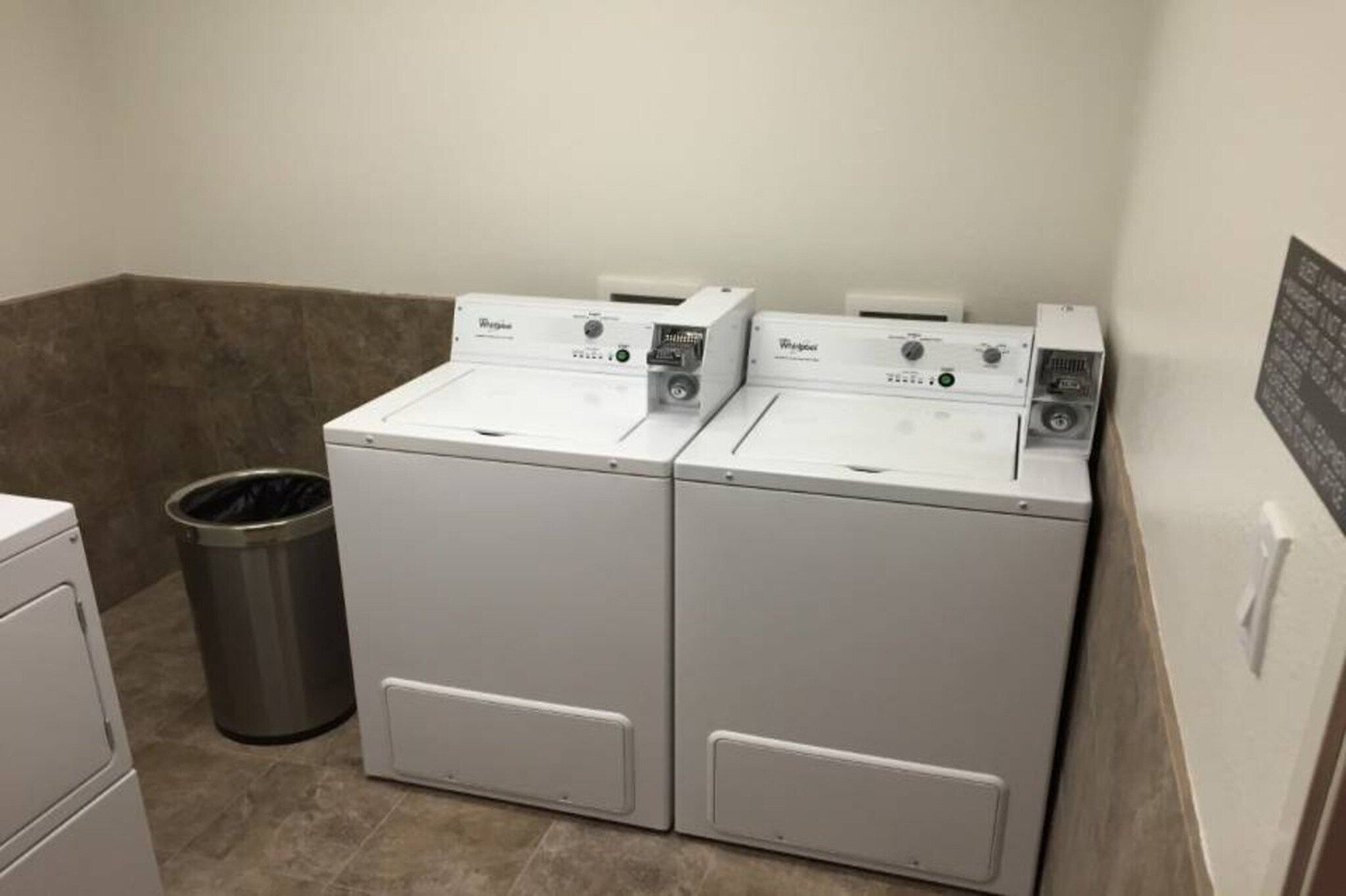 A laundry room with two front-loading washing machines and a metal trash can.