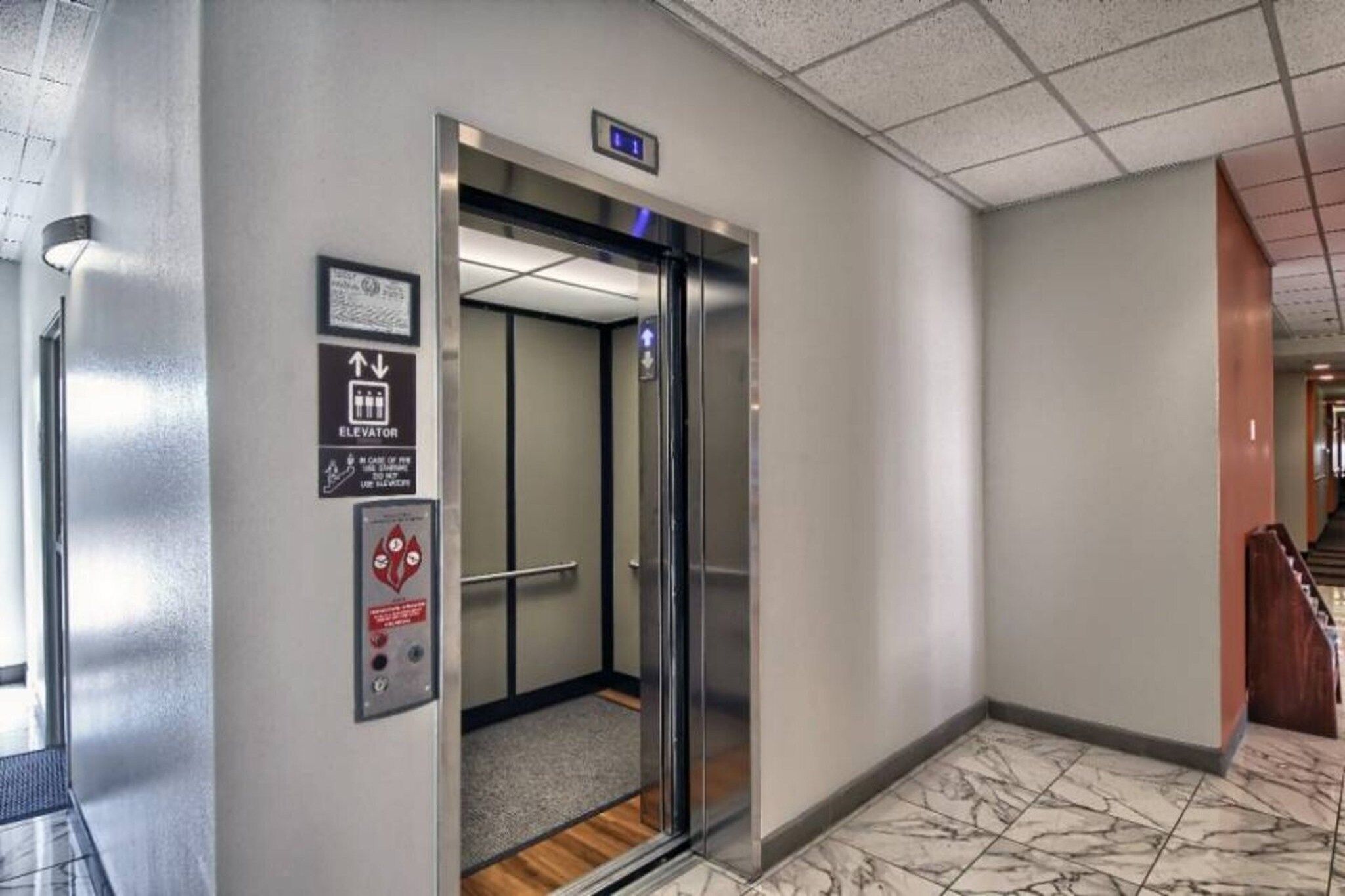 An elevator with a digital display, emergency instructions, and a handrail.