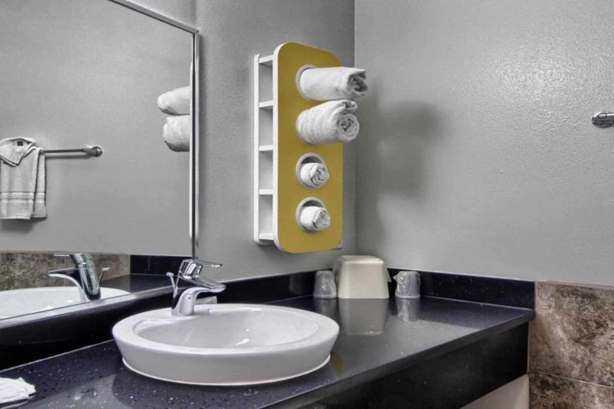 A bathroom with a white sink, a mirror, a towel rack, and a toilet paper holder.