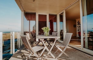 An outdoor balcony with a table and chairs, a glass door leading to an interior space, and a view of the beach. - Luxury coastal apartment Crab in Egmond aan Zee for 6 guests, with 3 bedrooms, a balcony and panoramic sea views. (Egmond aan Zee)