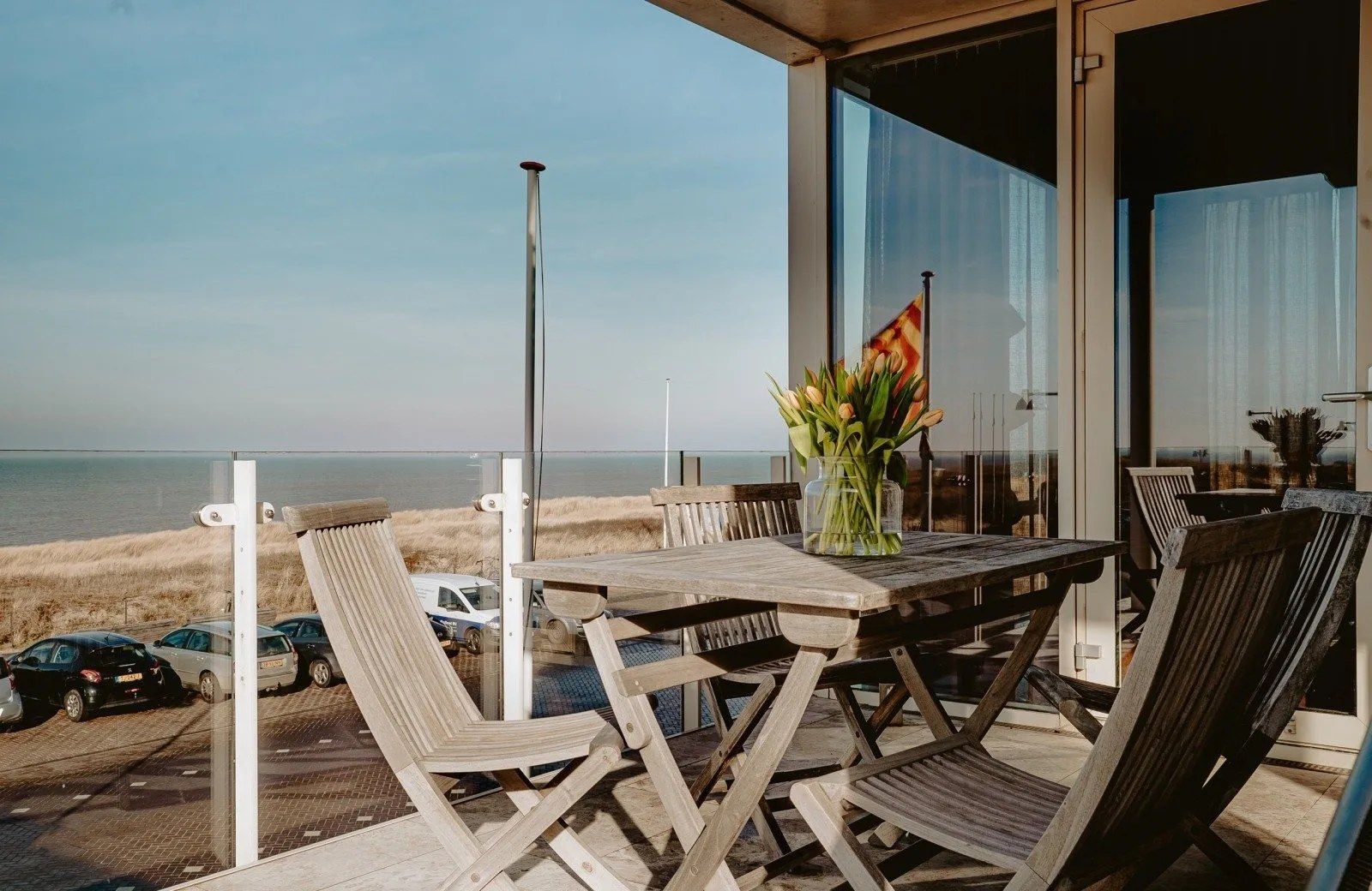 A wooden table and chairs on a balcony with a view of the beach and ocean.