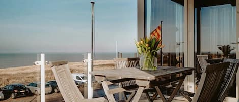 A wooden table and chairs on a balcony with a view of the beach and ocean.