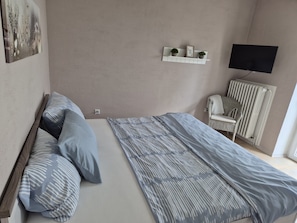 A bedroom with a bed, pillows, a chair, a radiator, and a wall-mounted TV. - Eifelglück House (Großlittgen)