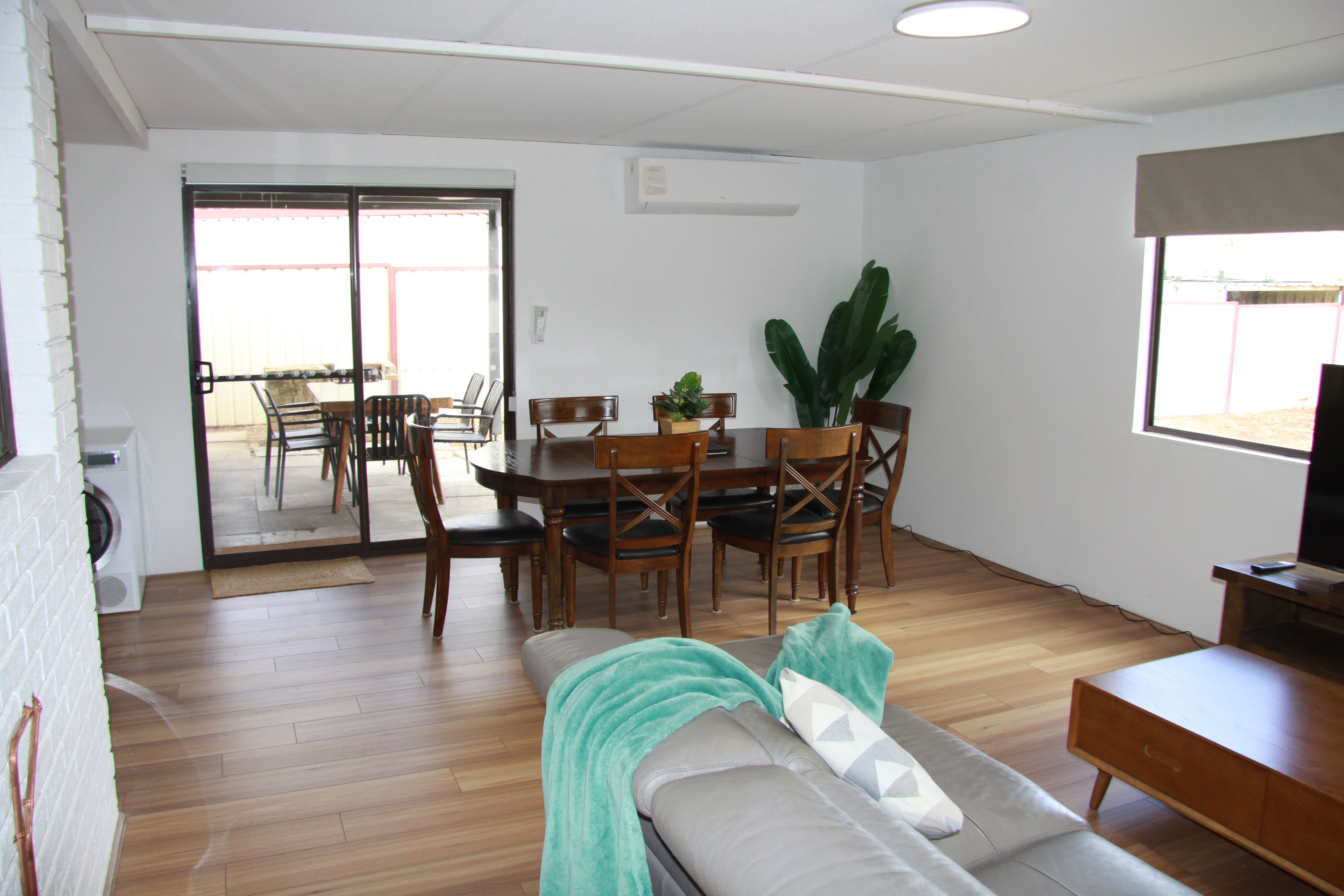 A living room with a sofa, a dining table with chairs, a TV stand, and a large window.
