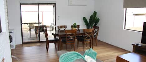 A living room with a sofa, a dining table with chairs, a TV stand, and a large window.