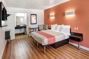 Une chambre d’hôtel moderne, équipée d’un lit, de tables de chevet, d’un bureau et d’une salle de bain visible à travers une porte ouverte.