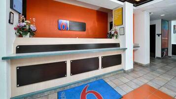 A reception desk with a logo, a blue carpet with a red '6', and a flower arrangement.