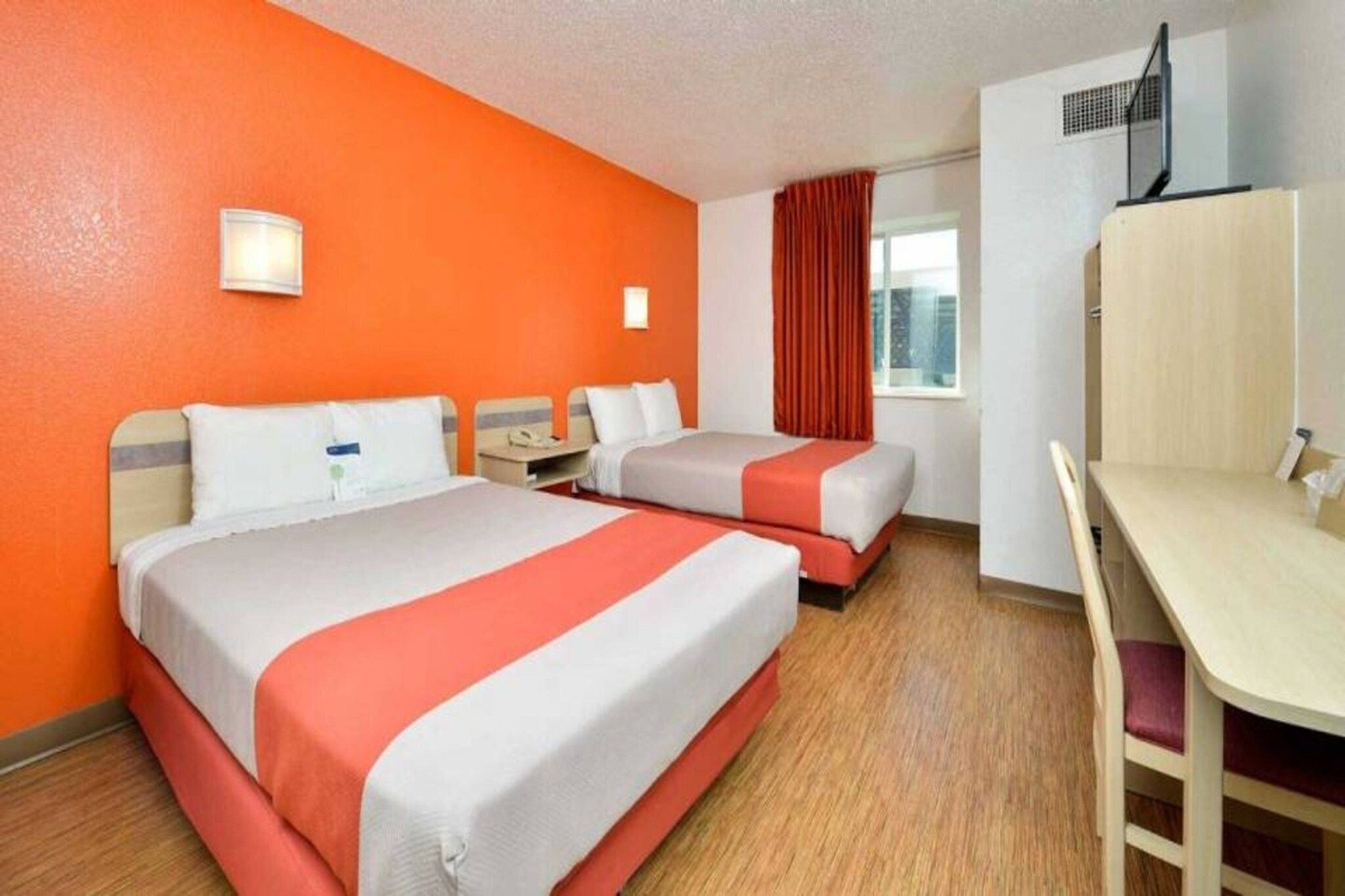 A hotel room with two beds, a desk, and a window with curtains.