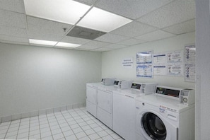 Une buanderie équipée de quatre machines à laver, d’un sèche-linge et de panneaux d’information accrochés au mur.