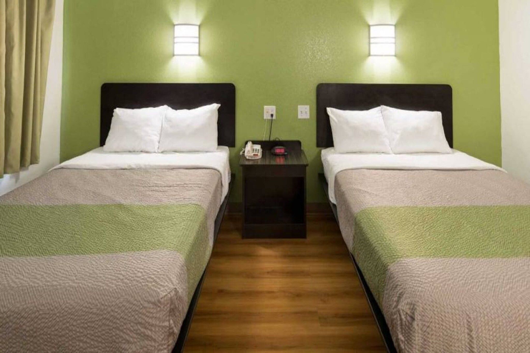 A hotel room with two beds, a nightstand, and a green wall.