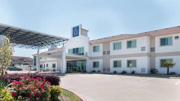 A hotel with a large parking lot, a covered entrance, and a clear sky.