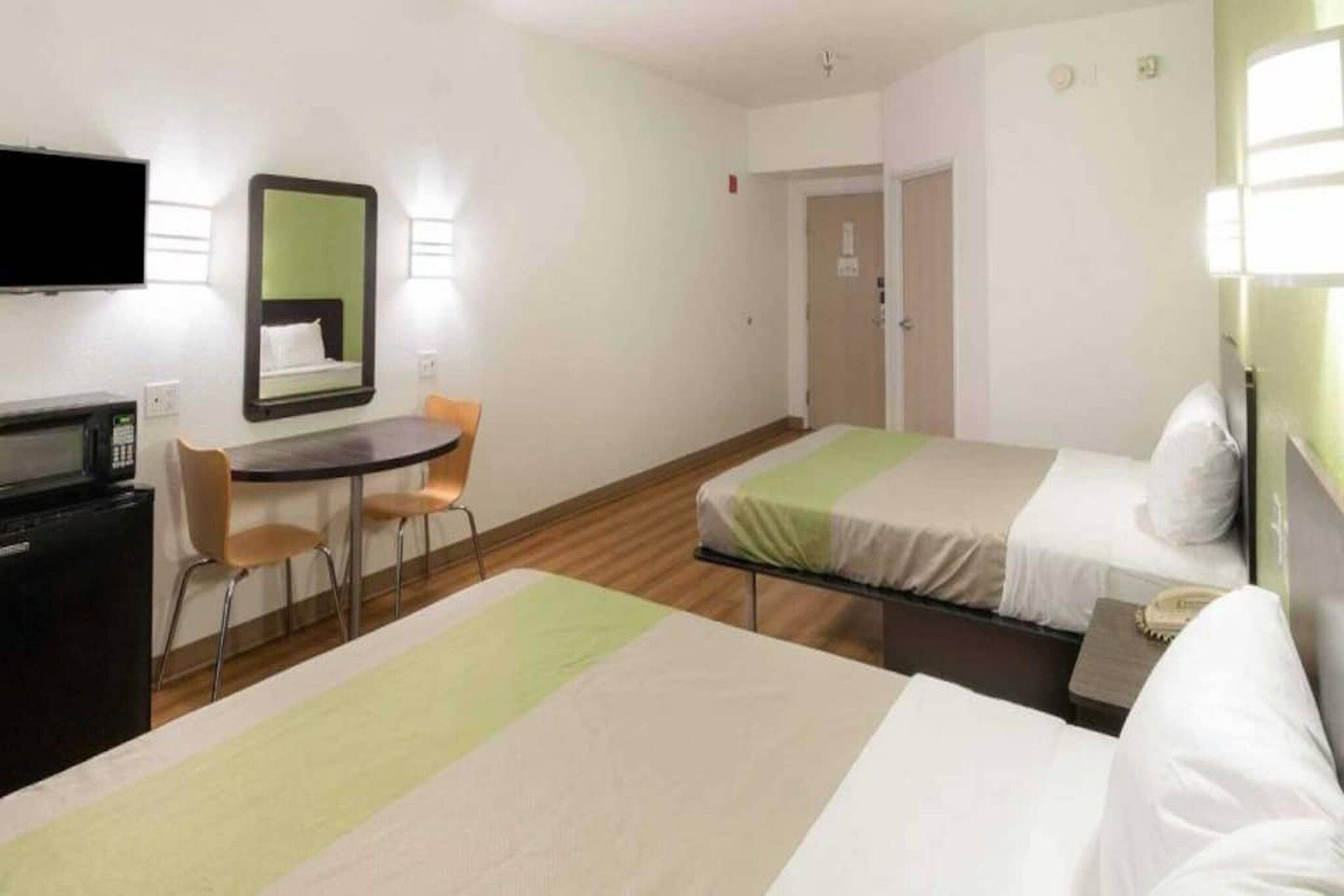 Habitación de hotel con dos camas, un escritorio con silla, televisión y espejo.