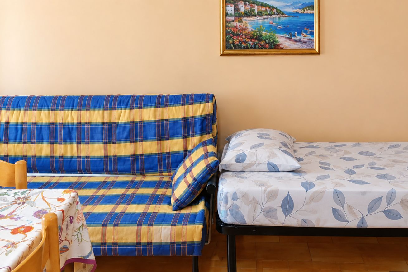 Ein Zimmer mit einer Couch und einem Bett, einem Bild an der Wand und einem Tisch mit einer blumigen Tischdecke.
