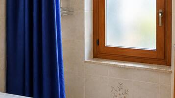 Un baño con cortina de ducha azul, ventana con marco de madera y pared de azulejos con diseño floral.