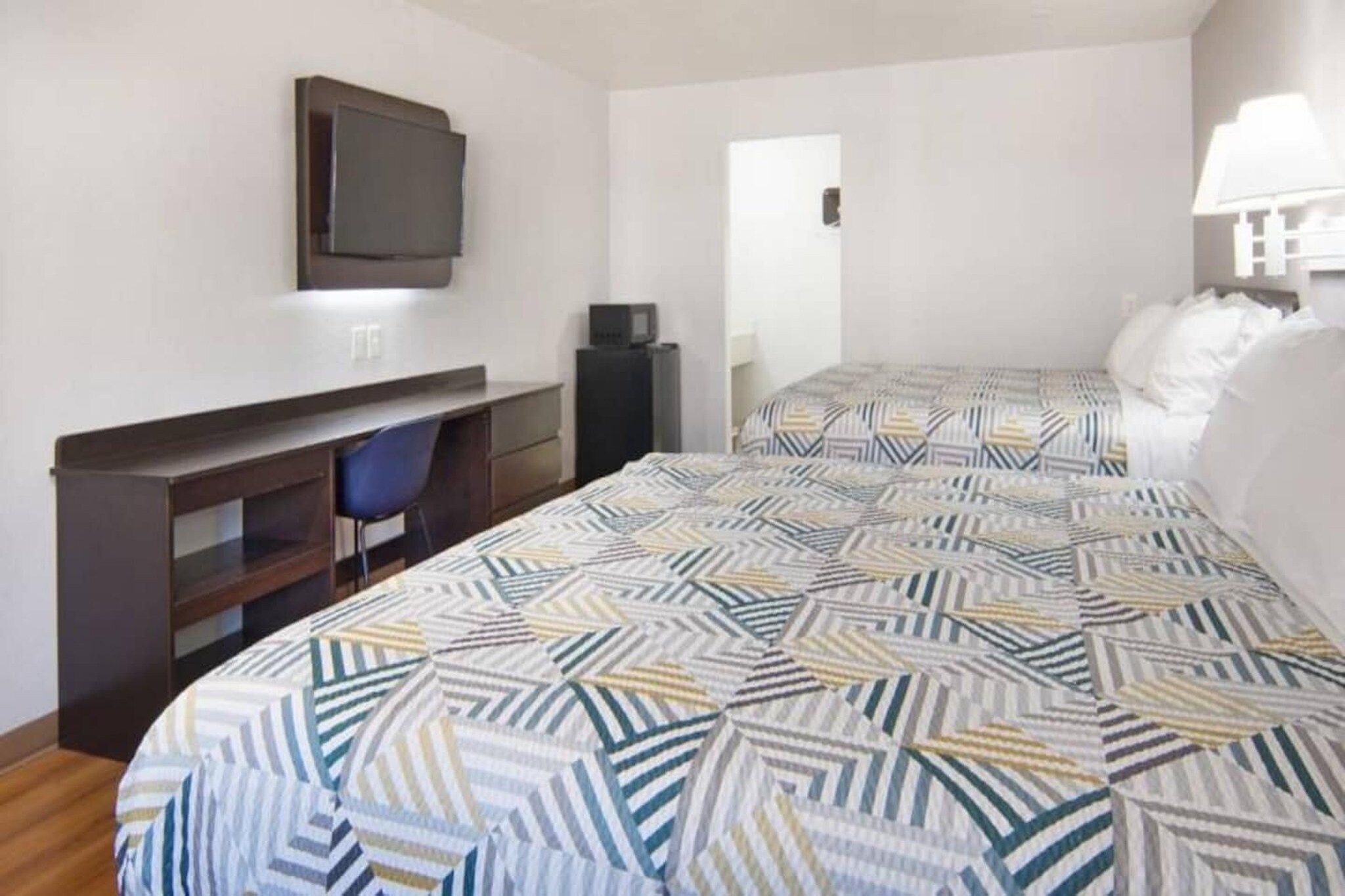 Une chambre d’hôtel avec un lit, un bureau, une chaise, une télévision et une porte.