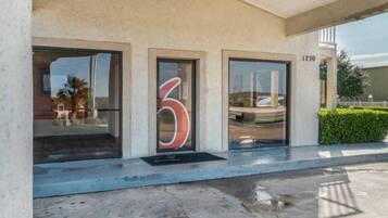 A building entrance with a large number '6' on the door, a concrete ramp leading up to the entrance, and a street view visible through the windows.