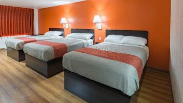 A hotel room with three beds, each with a headboard, a red wall, and a wooden floor.