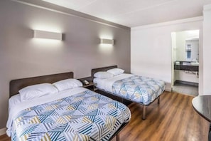 A hotel room with two beds, a small table, and a bathroom visible through an open door. - 2 Full Beds | Smoking (Dallas)
