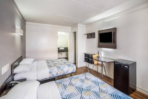 A hotel room with two beds, a desk, a chair, a TV, and a small kitchenette. - 2 Full Beds | Smoking (Dallas)