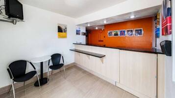 A small reception area with a counter, two chairs, a table, and a wall-mounted TV.