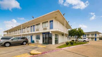 A multi-story motel with a flat roof, a central entrance, and a parking lot with marked spaces.