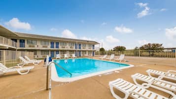 A motel with a swimming pool, multiple lounge chairs, and a fenced area.