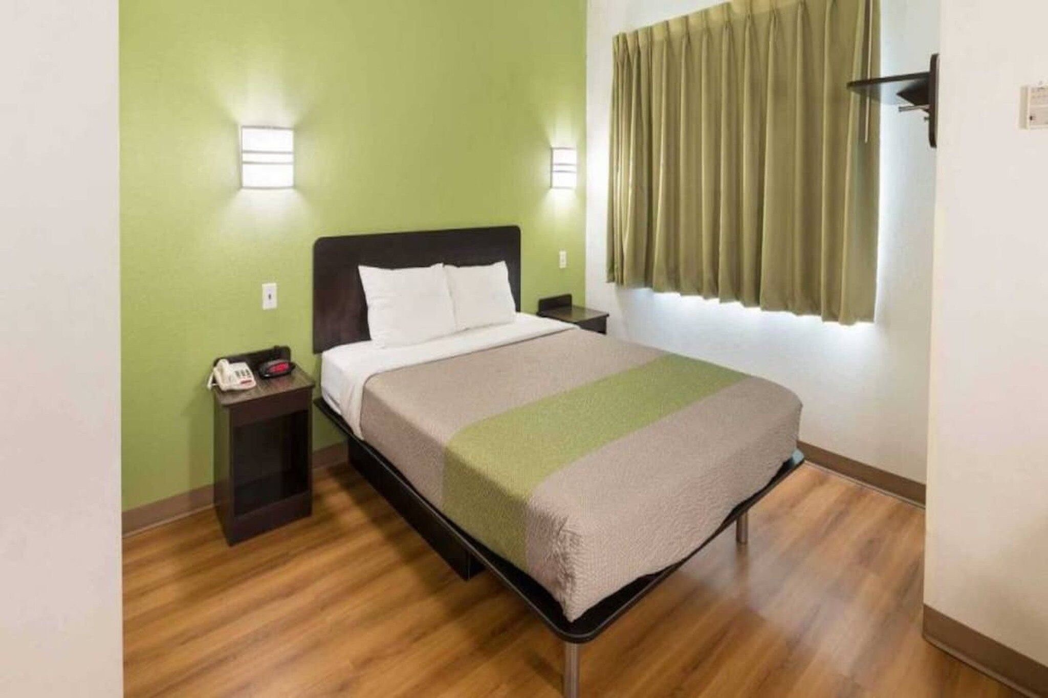 Una cama individual con cabecera, una mesita de noche con teléfono y una lámpara de pared.