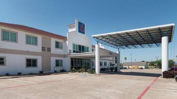 Un hotel con ingresso coperto, parcheggio e cielo azzurro.