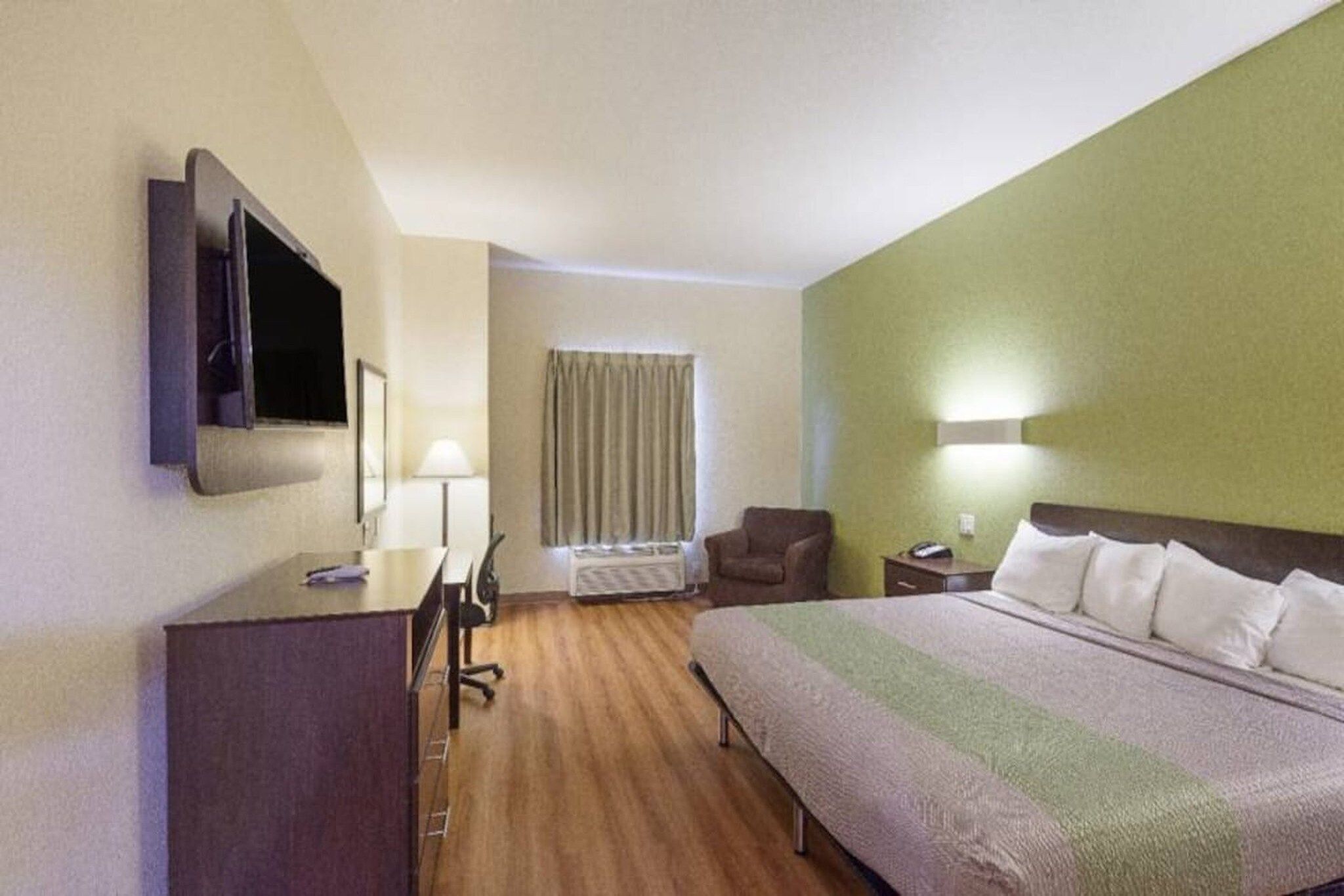 A hotel room with a bed, a desk with a chair, a television, a lamp, and a window with curtains.