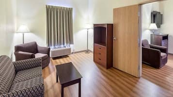 A hotel room with a sofa, a small table, a cabinet, a desk, a lamp, a window with curtains, and a television.