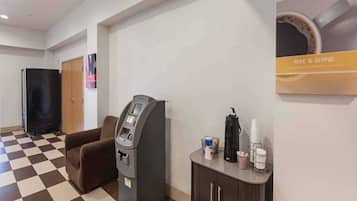 A hotel lobby with a check-in kiosk, a seating area, and a coffee station.