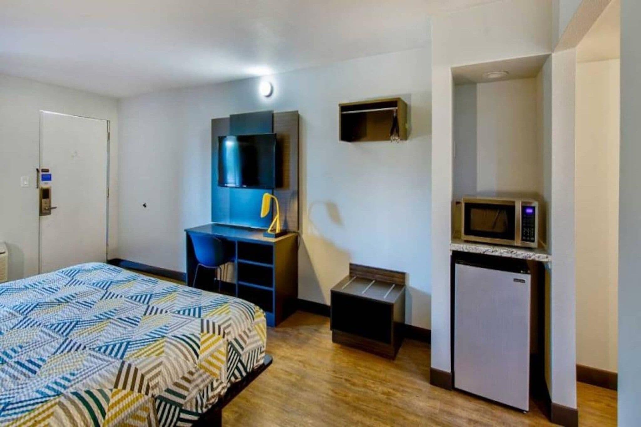 Une chambre d’hôtel équipée d’un lit, d’un bureau, d’une chaise, d’un four à micro-ondes et d’un petit réfrigérateur.