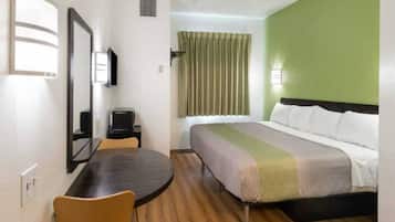 Habitación de hotel con cama, escritorio, silla, televisor y ventana con cortinas.