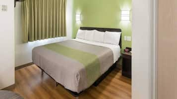Una habitación de hotel con una cama, una mesita de noche, una lámpara y un ventanal con cortinas.