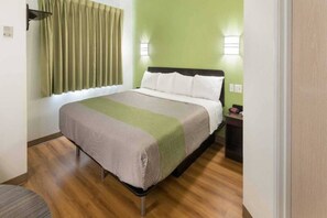 Una habitación de hotel con una cama, una mesita de noche, una lámpara y un ventanal con cortinas.