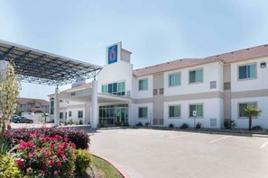 Un hotel con estacionamiento techado, una entrada amplia y un edificio con múltiples ventanas.