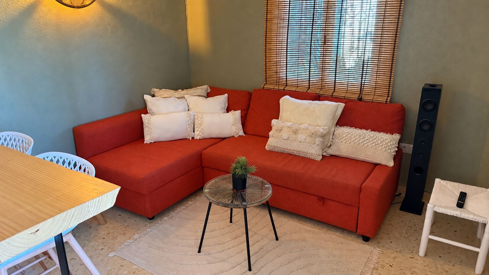 A red sectional sofa with multiple cushions, a small round table with a plant, a white chair, and a tall speaker unit.