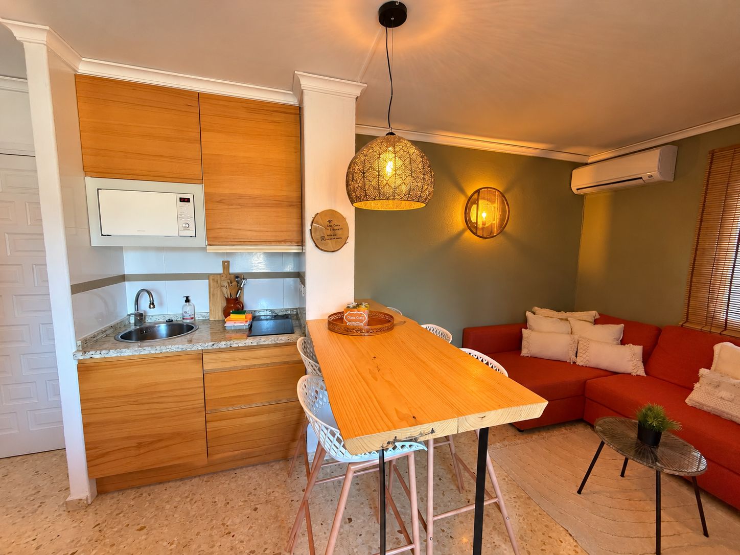 Una cocina compacta con encimera de madera, un taburete de bar y una lámpara colgante.