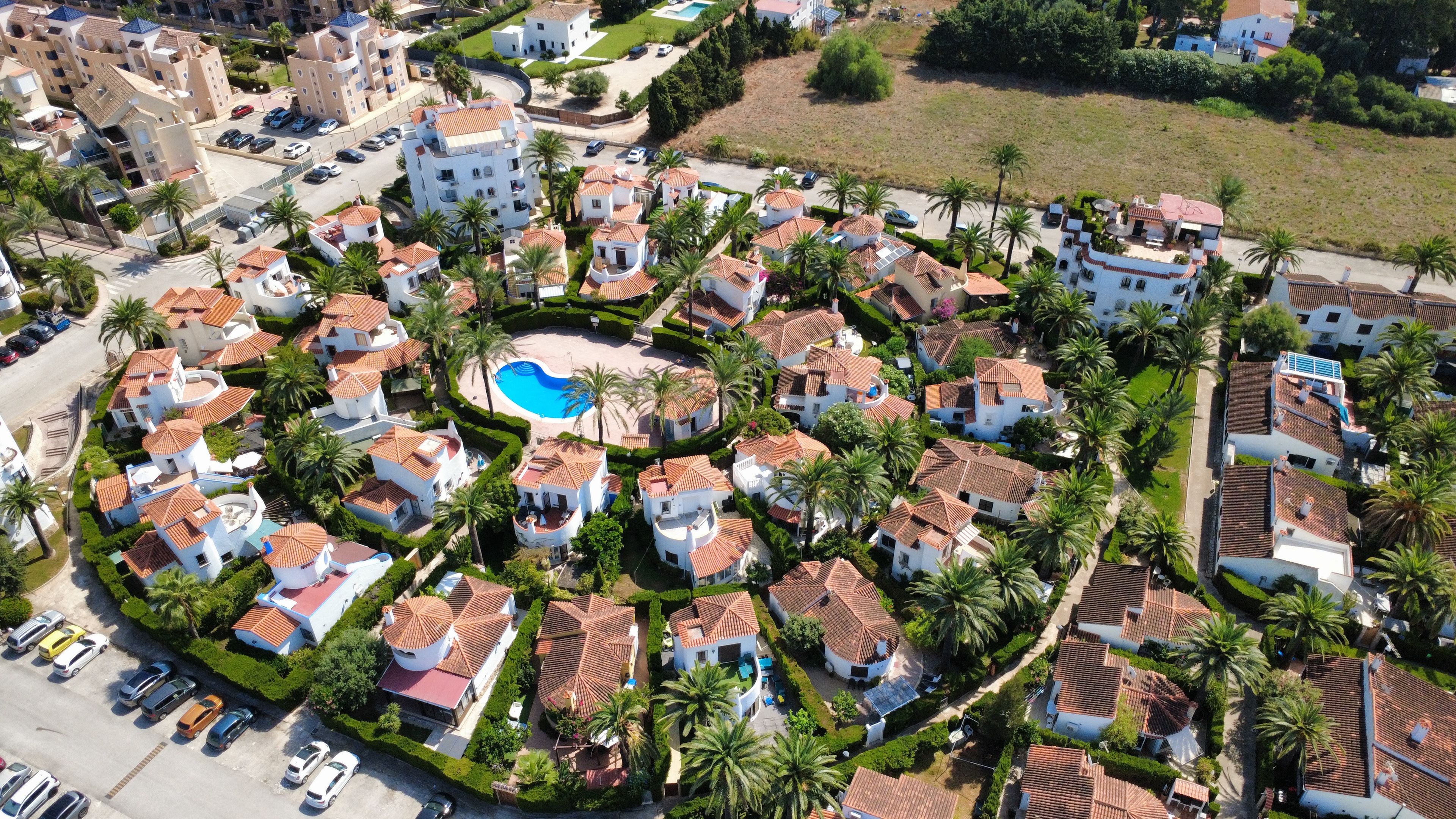A residential area with multiple houses, a swimming pool, and parked cars.