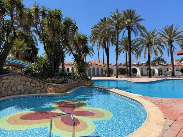 A swimming pool with a colorful mosaic design, surrounded by palm trees and a stone wall. - 2 slaapkamer appartement Denia (Denia)